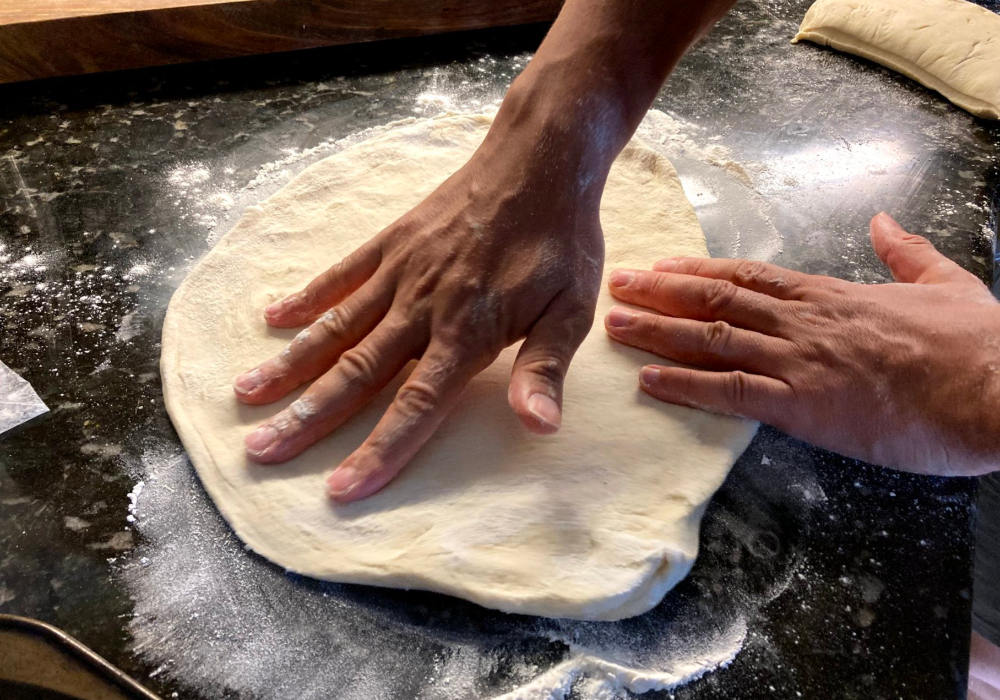 Mens hands shaping a round of uncooked pizza dough in preparation to put vegan white pizza toppings.
