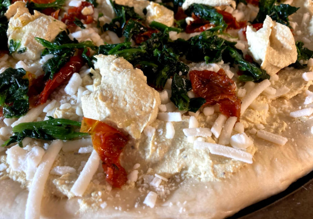 Vegan white pizza with spinach, sun-dried tomatoes and vegan ricotta pre-bake.