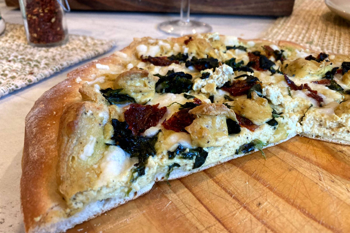 Vegan white pizza with tofu ricotta, spinach and sun-dried tomato on a cutting board.