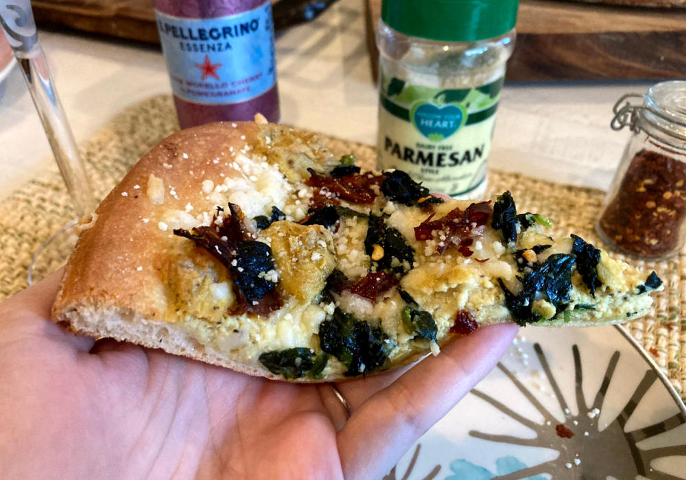 Vegan white pizza slice with tofu ricotta, spinach and sun-dried tomatoes topped with parmesan and paired with Pellegrino.