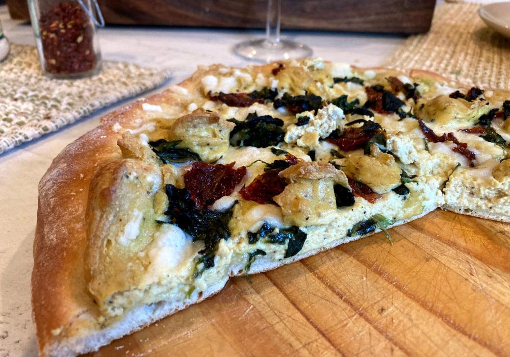 Vegan white pizza with tofu ricotta, spinach and sun-dried tomatoes sliced on a cutting board.