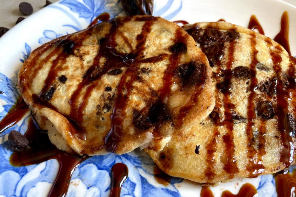 Vegan chocolate chip pancakes on a blue and white floral plate drizzled with date syrup.