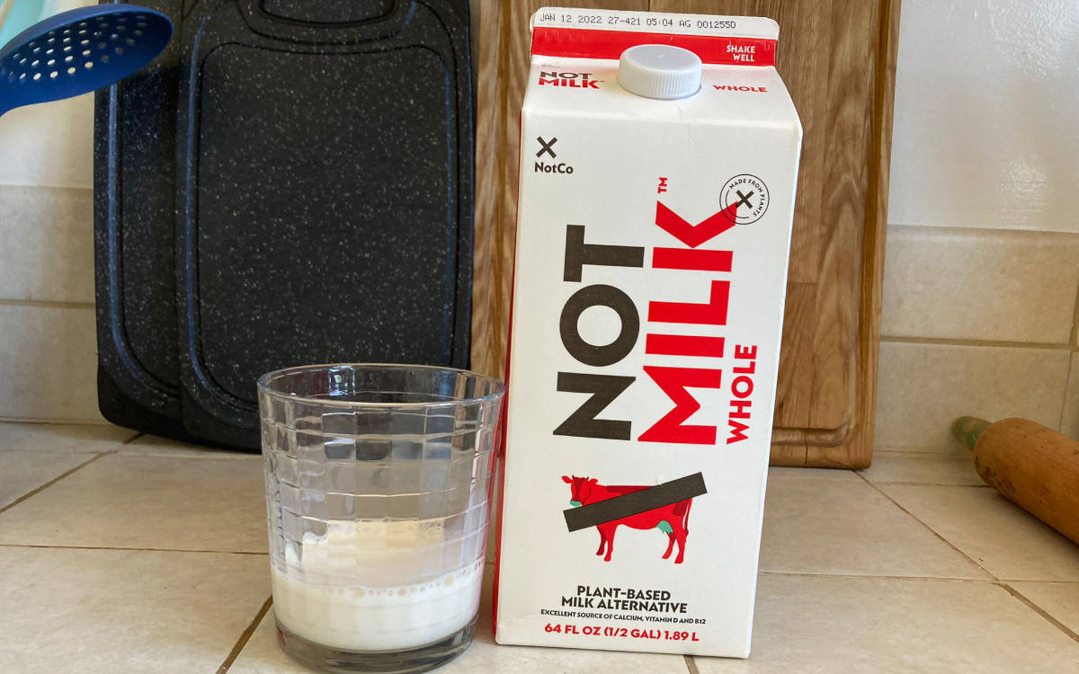 Carton of whole Not Milk with a sip in a clear glass on a tile counter.