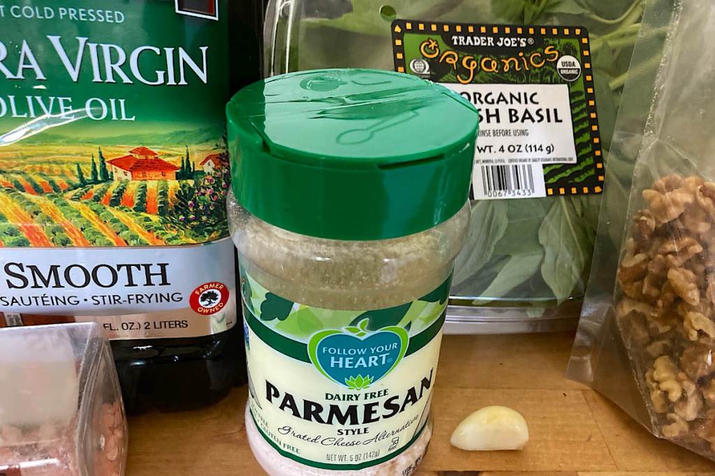 Vegan pesto ingredients like olive oil, garlic, vegan parmesan, basil and walnuts.