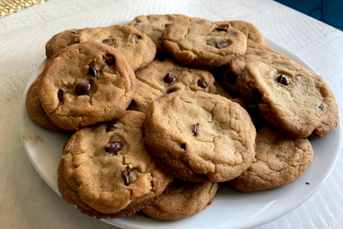 A plate full of vegan chocolate chip cookies, tollhouse style on a distressed white wooden table/