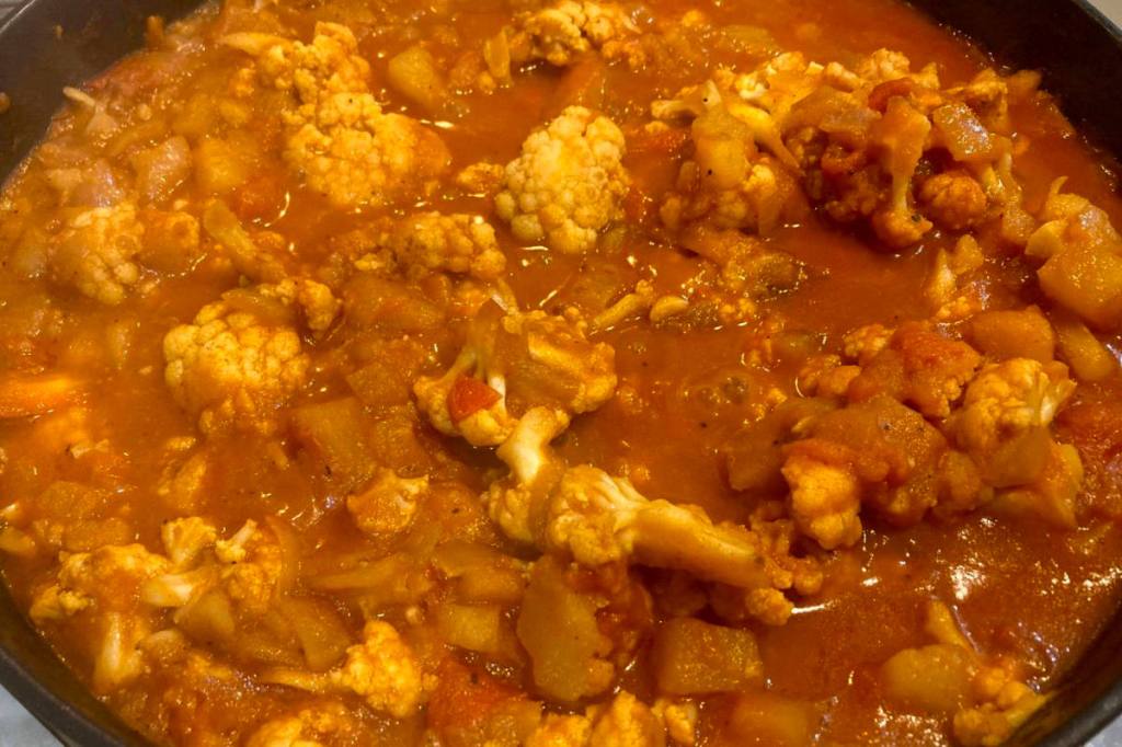Creamy vegan aloo gobi in a pan with a tomato and coconut cream gravy