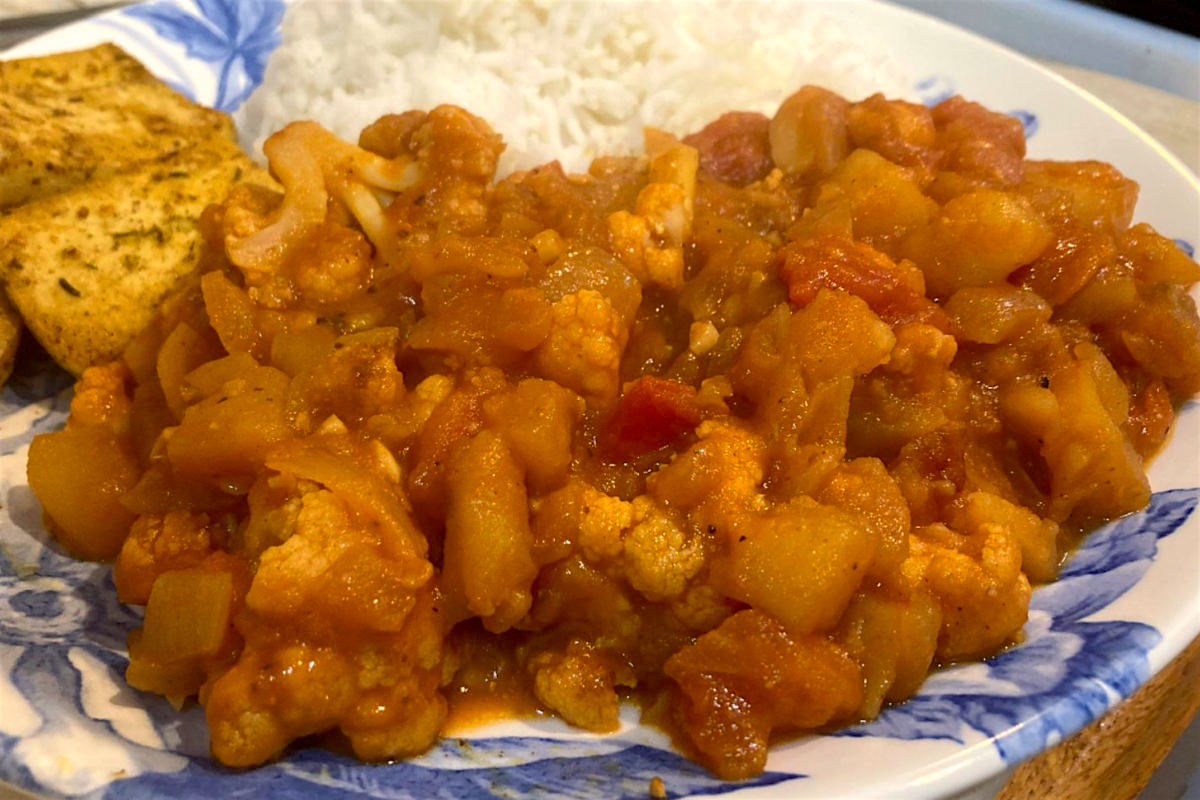 Vegan aloo gobi, an Indian dish featuring cauliflower and potatoes, on a blue and white plate.